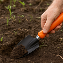 Load image into Gallery viewer, Hand holding an orange-handled trowel with soil in a garden setting