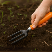 Load image into Gallery viewer, Hand holding a small garden fork with an orange handle in soil
