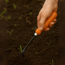 Load image into Gallery viewer, Hand holding an orange-handled garden tool in soil with young plants
