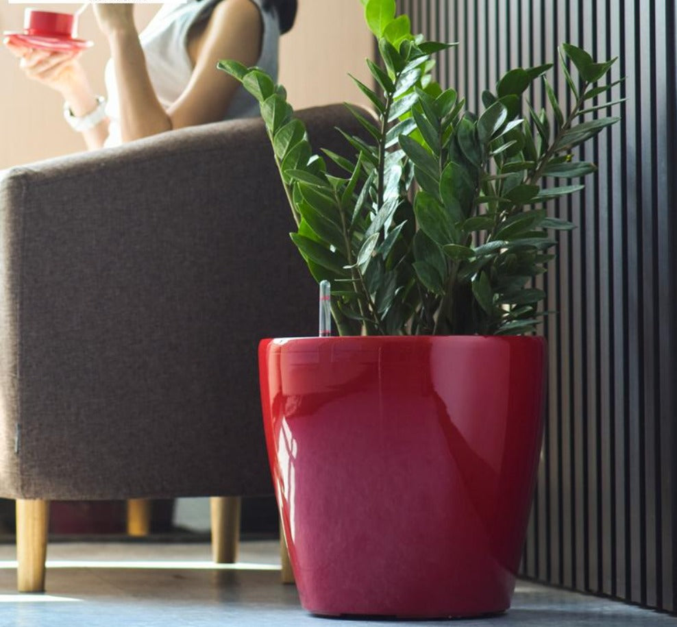 A red, round, glossy pot planter with a person sitting in the background, indoors.